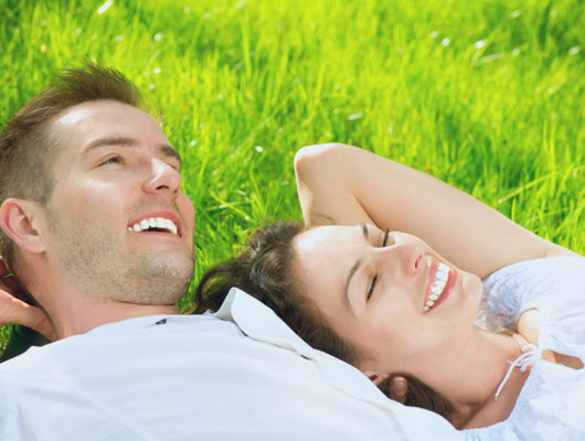 Zwei Personen lachend und liegend auf der Wiese bei herrlichem Wetter
